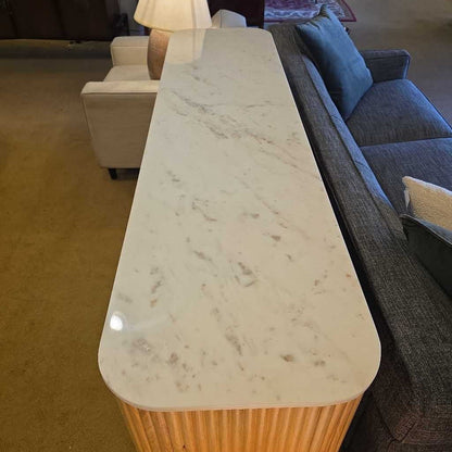 Marble-top coffee table in a living room setting with a sofa and lamp in the background.