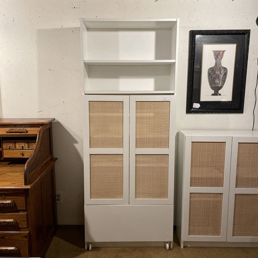 White cabinet with wicker doors next to a wooden desk and framed picture on a wall.