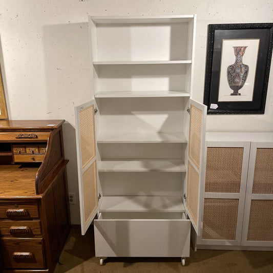 White cabinet with wicker doors in a room with wooden furniture and a framed picture on the wall.