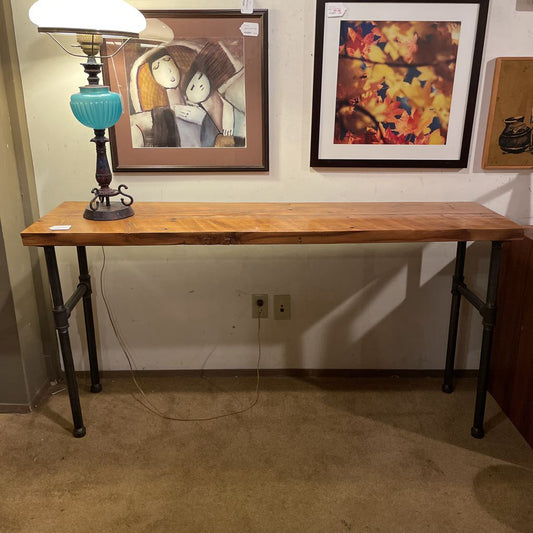 Wooden table with a lamp and framed pictures on a wall.