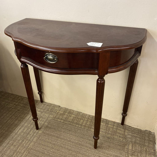 Wooden half-moon table with a dark finish against a plain wall.