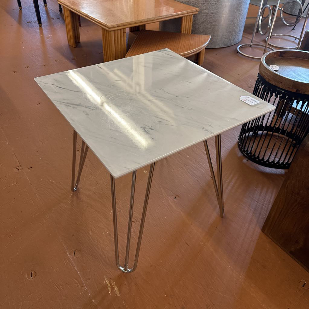 Square table with marble-like top and metal legs on a wooden floor.