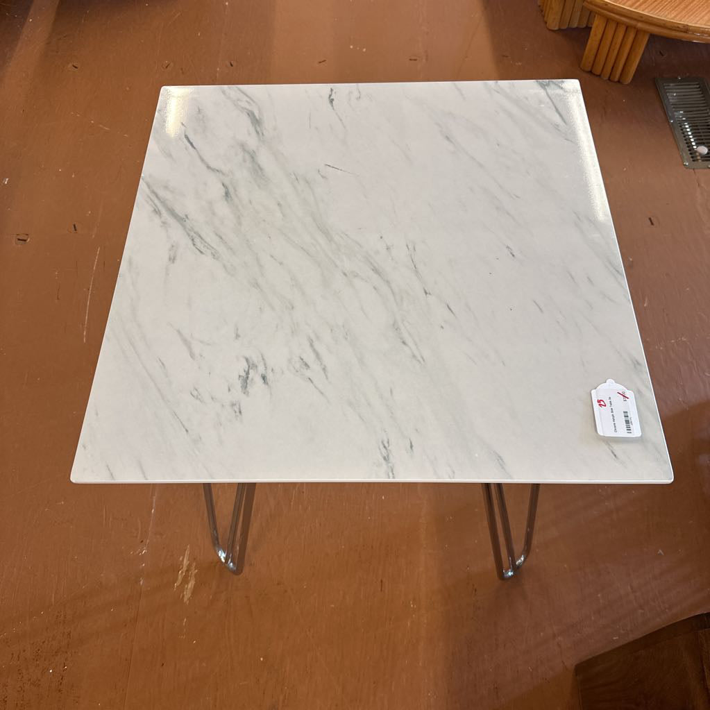 Small square table with marble-like top and metal legs on a brown surface