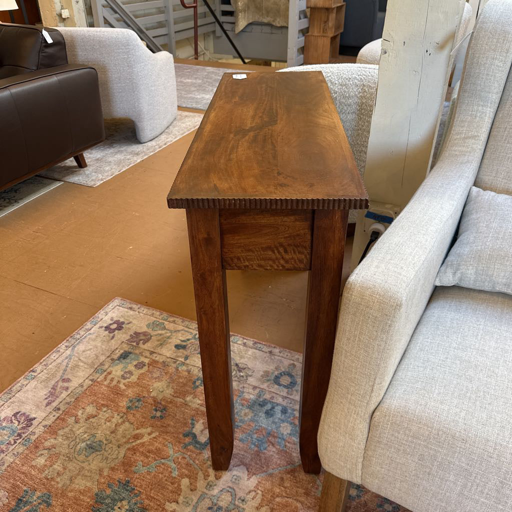 Wooden side table in a room with furniture and a patterned rug.