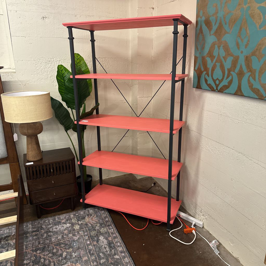 Red shelf with black metal legs in a room with a lamp, plant, and wall art.