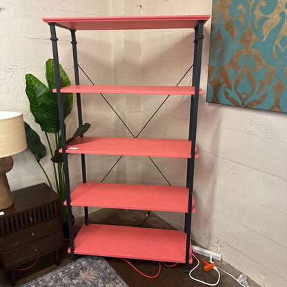 Red shelf with black metal legs against a wall with a painting