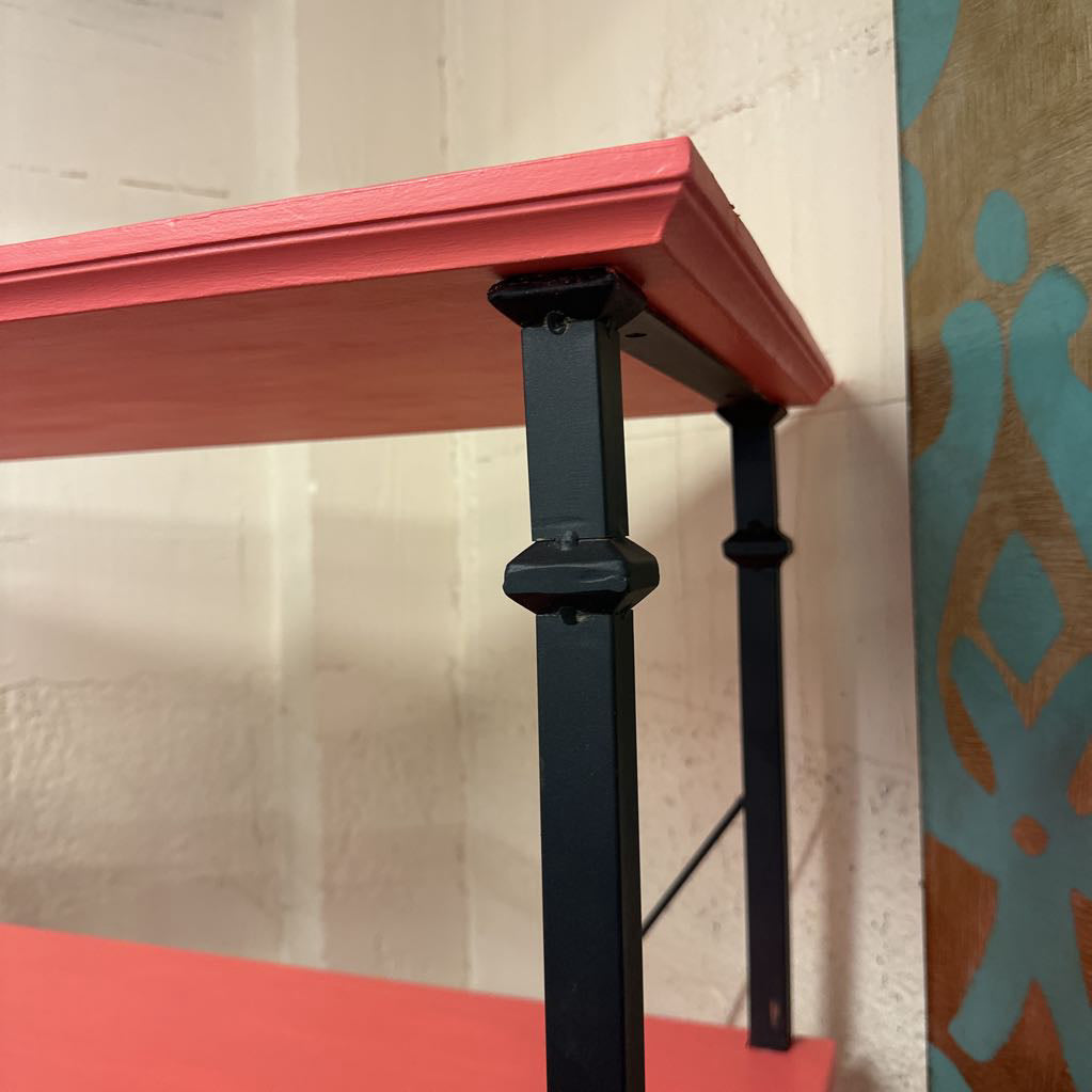 Red table with black metal legs against a textured wall.