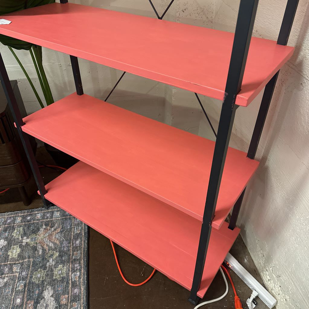 Red shelf with black metal legs against a wall.