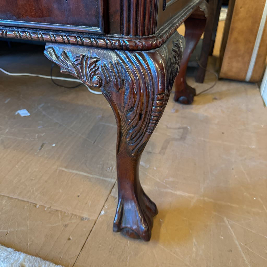 Carved wooden leg of a piece of furniture on a wooden floor.