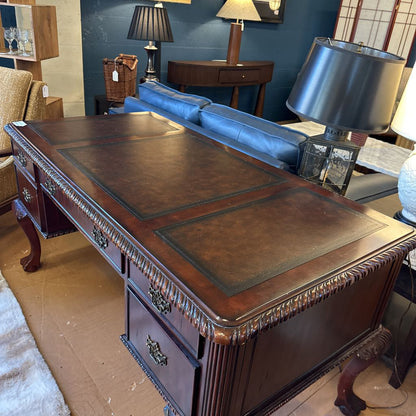 Vintage wooden desk with leather surface in a room with lamps and furniture.