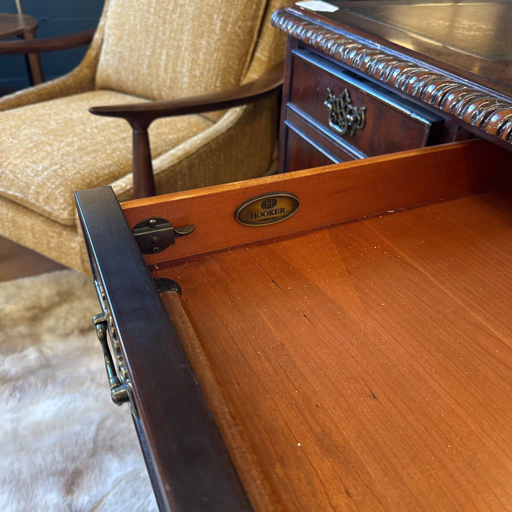 Wooden desk with open drawer, showing a brand logo, in an indoor setting.