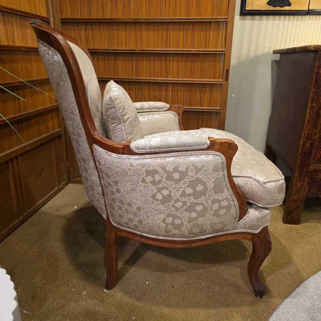 Decorative armchair with patterned fabric and wooden frame in a room with bookshelves.