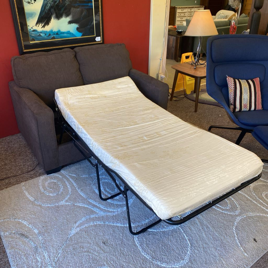 Sofa bed extended in a room with a red wall, lamp, and chair.