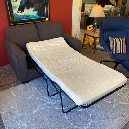 Sofa bed extended in a room with a red wall, lamp, and chair.