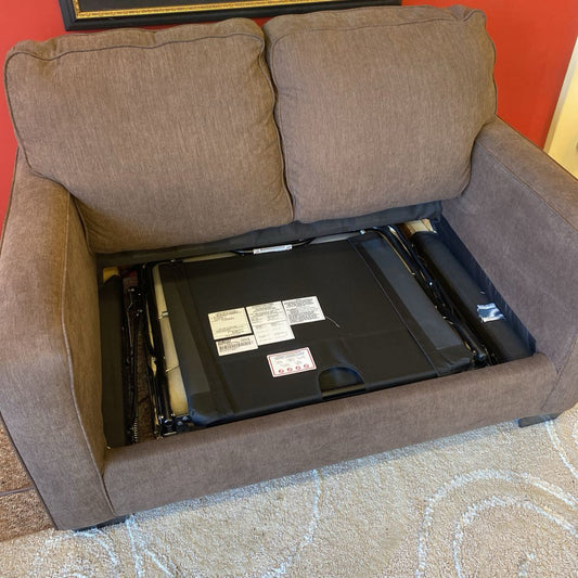 Brown sofa with a black electronic device underneath on a patterned carpet.