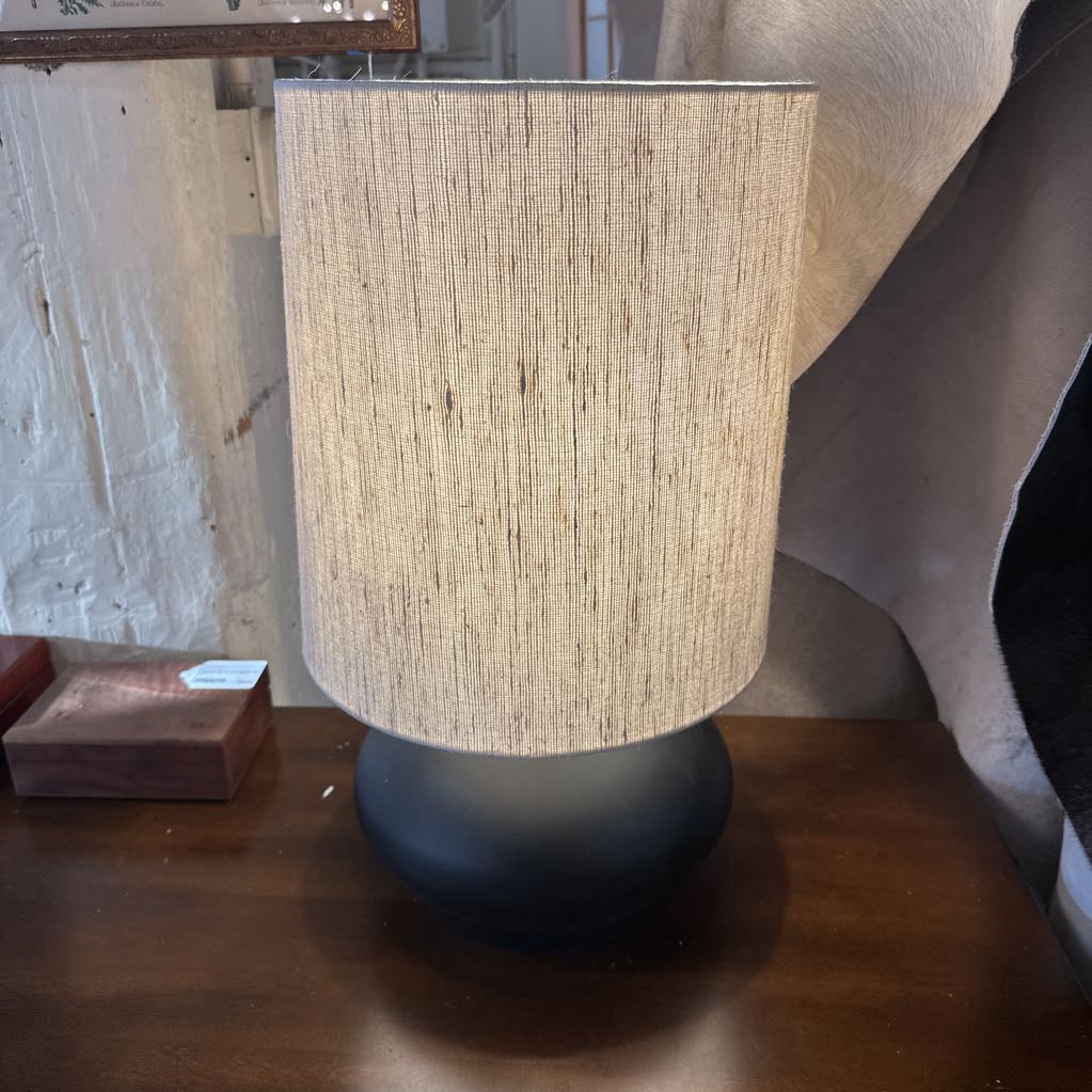 Table lamp with a textured beige shade and black base on a wooden surface.