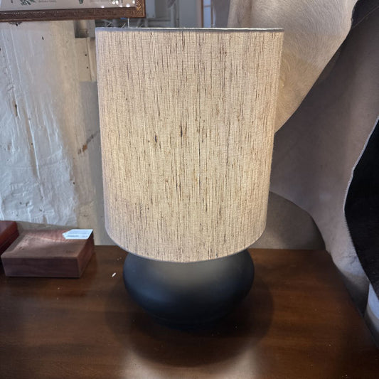 Table lamp with a textured beige shade and black base on a wooden surface.