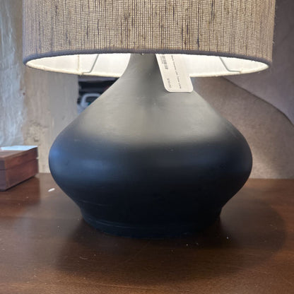 Black table lamp with a textured gray shade on a wooden surface.