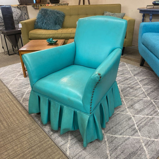 Turquoise chair with a skirted design in a room with a green sofa and wooden coffee table.