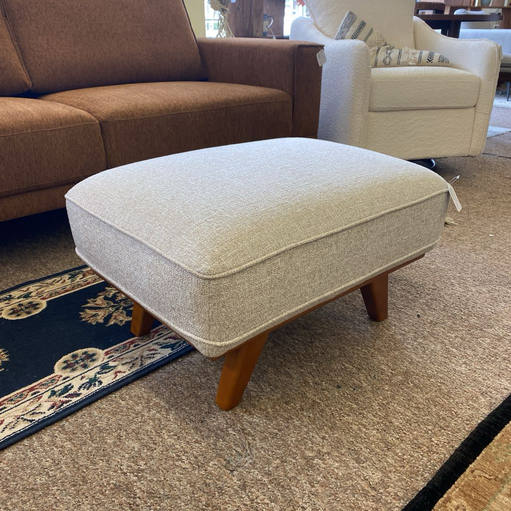 Beige ottoman with wooden legs in a living room setting