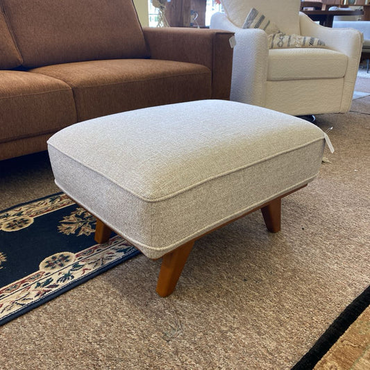 Beige ottoman with wooden legs in a living room setting