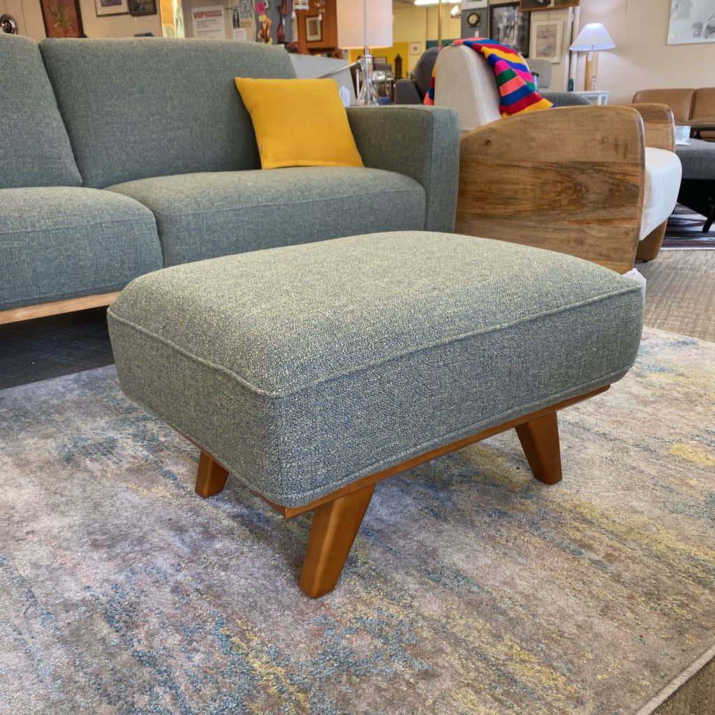 Gray upholstered ottoman in a room with furniture and decor.