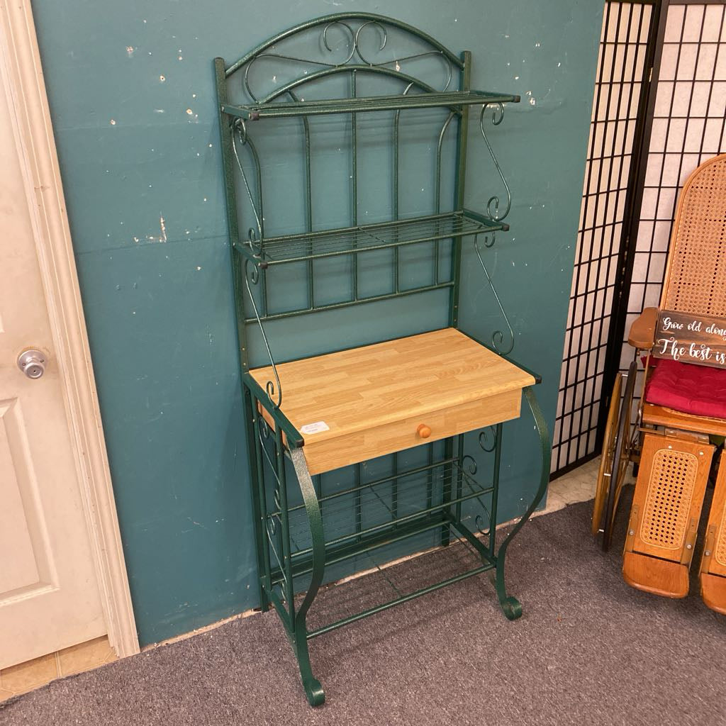 Green metal baker's rack with wooden shelf against a teal wall.