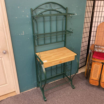 Green metal baker's rack with wooden shelf against a teal wall.