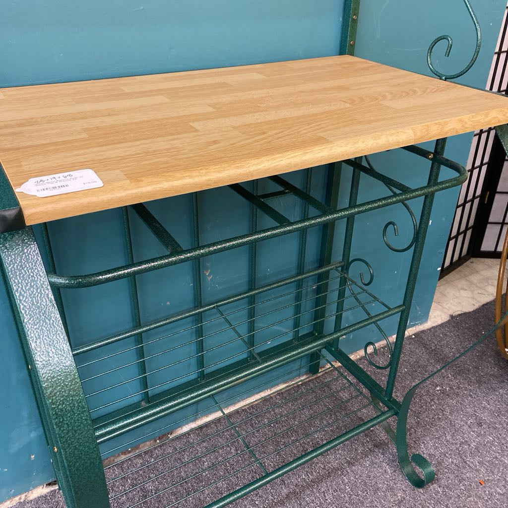 Green metal baker's rack with a wooden top against a blue wall.