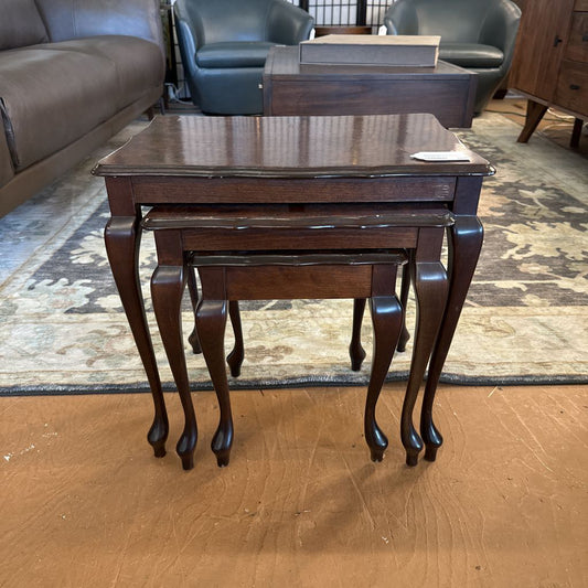Set of three dark wood nesting tables on a wooden floor with furniture in the background.