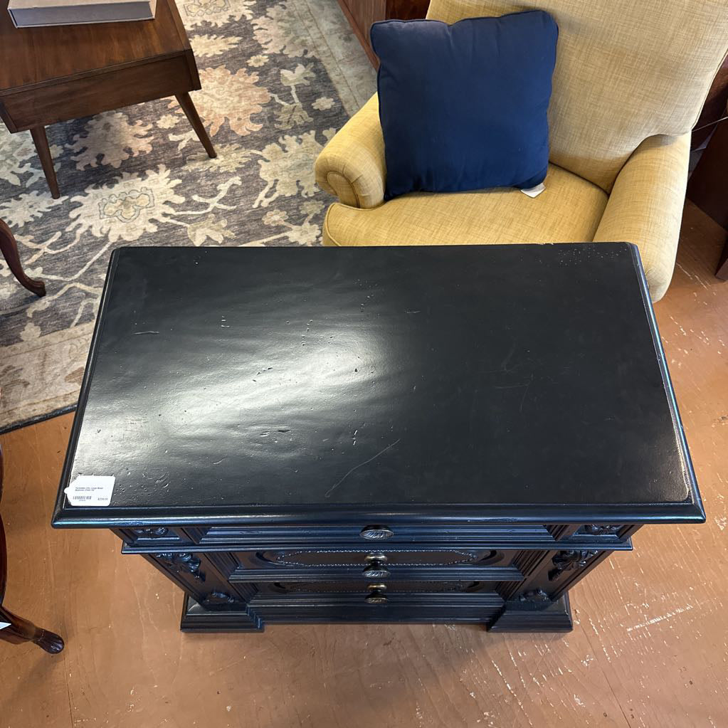 Black wooden side table in a room with a beige armchair and blue pillow.