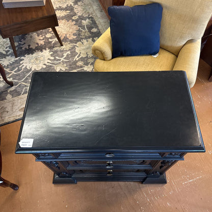 Black wooden side table in a room with a beige armchair and blue pillow.