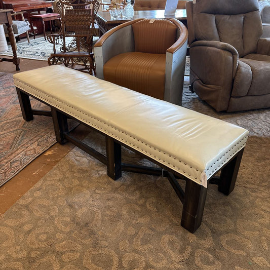 Long beige bench with dark wooden legs in a room with furniture and carpet.