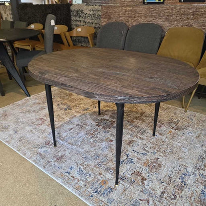 Wooden dining table with black legs on a patterned rug in a room with chairs and a couch.