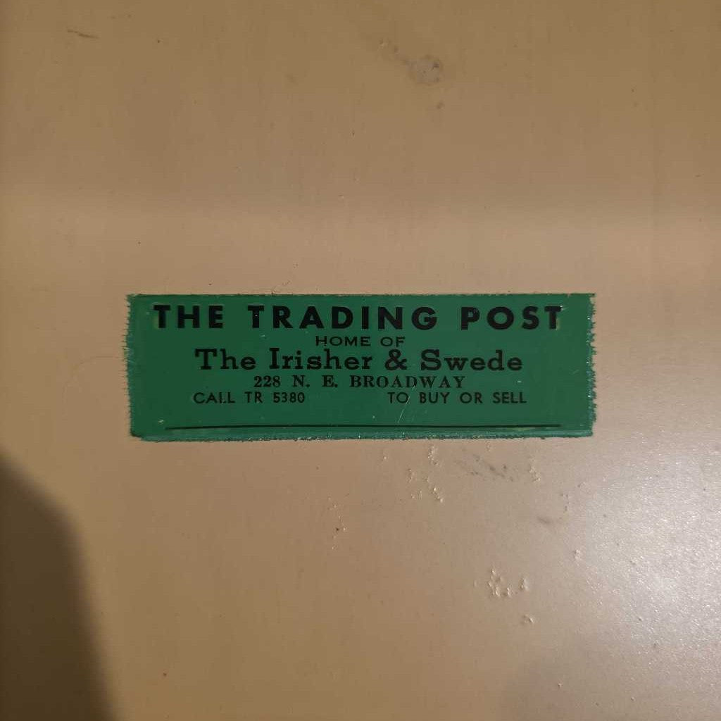 Green sign on a beige wall advertising 'The Trading Post' with contact information.