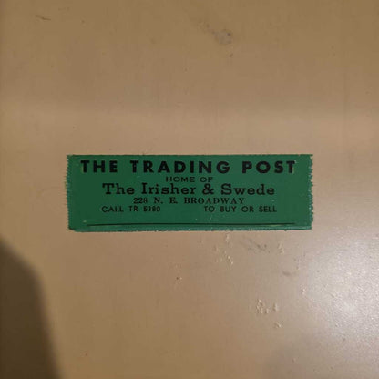 Green sign on a beige wall advertising 'The Trading Post' with contact information.