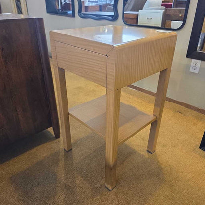 Wooden side table with a drawer and shelf in a room setting.