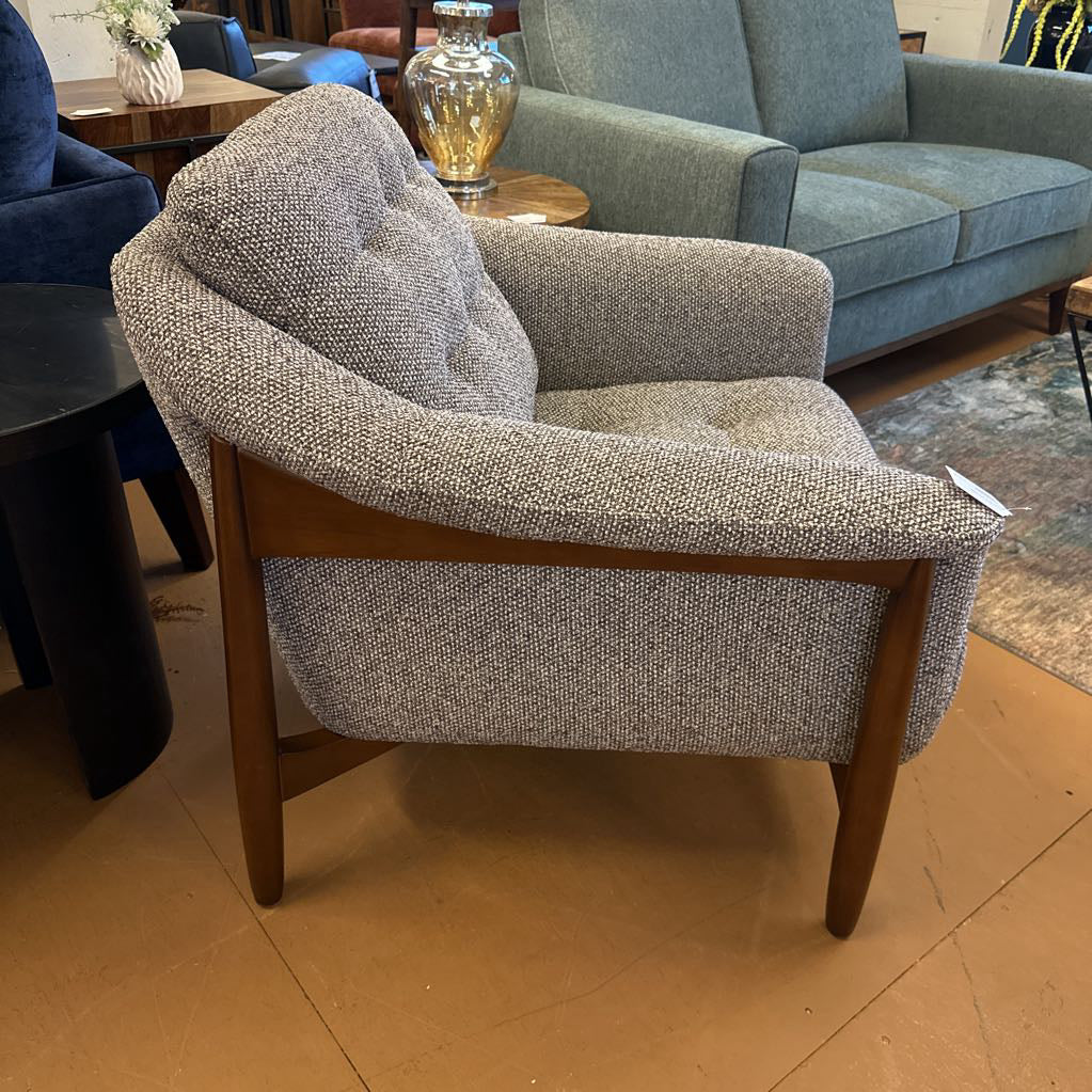 Gray armchair with wooden legs in a room with other furniture.