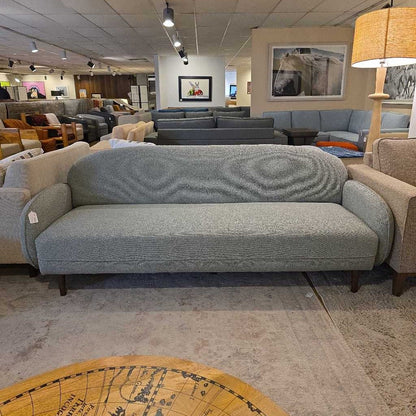 Gray sofa in a furniture store with various other furniture pieces in the background.