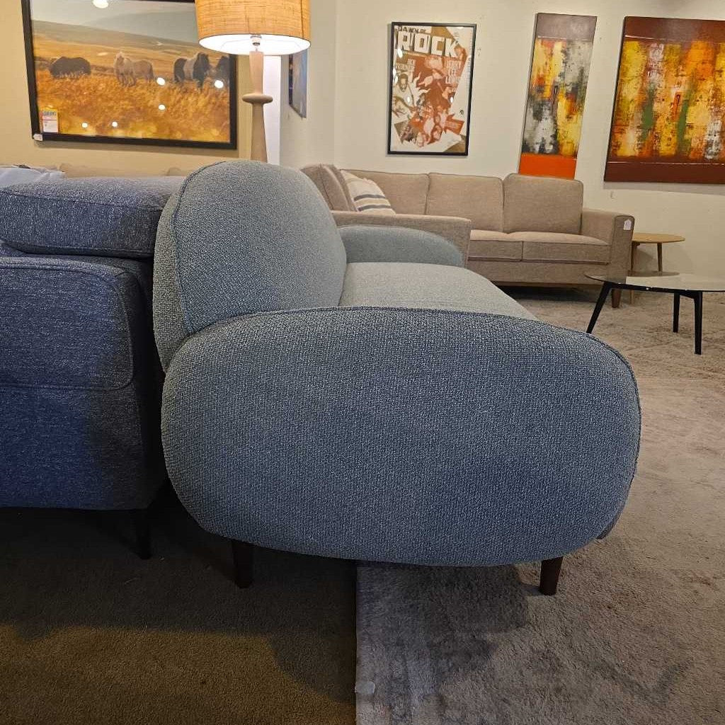 Blue sofa in a living room with a beige couch and colorful artwork on the walls.