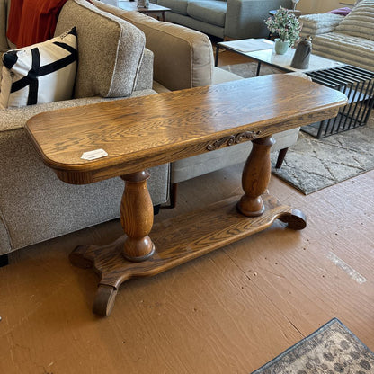 Wooden side table in a living room setting with a sofa and coffee table in the background.