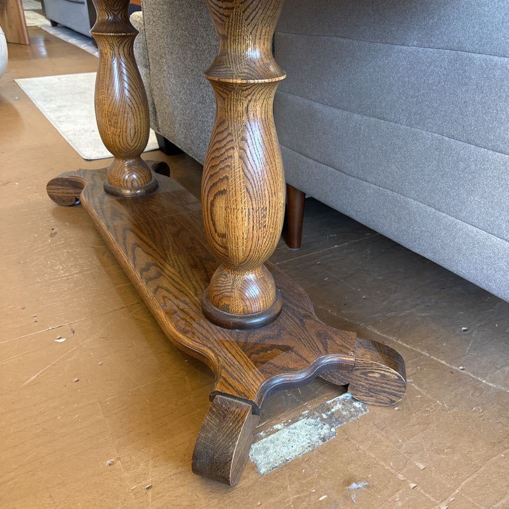 Wooden leg of a piece of furniture on a floor with a gray couch in the background