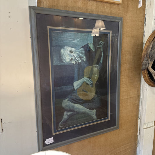 Framed artwork of a figure playing a guitar on a textured wall.