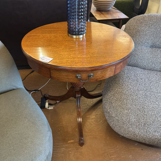 Round wooden side table with a glass vase on top, surrounded by gray chairs.