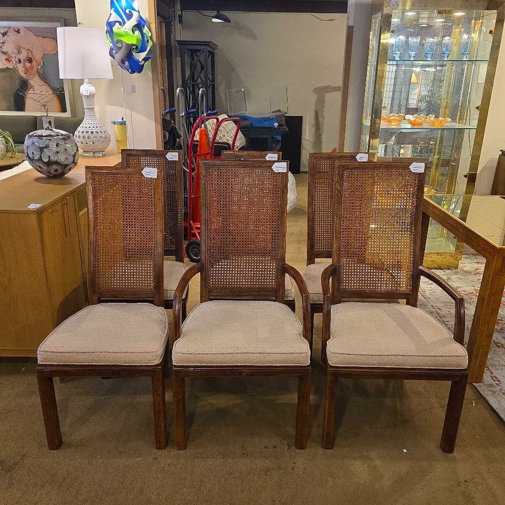 Set of four wooden chairs with cane backrests and beige cushioned seats in a room.