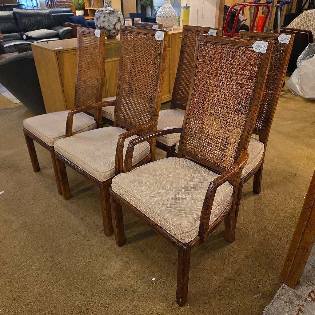 Set of four wooden chairs with wicker backrests and beige cushions in a showroom setting.