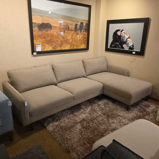 Beige sectional sofa in a room with framed pictures on the wall.