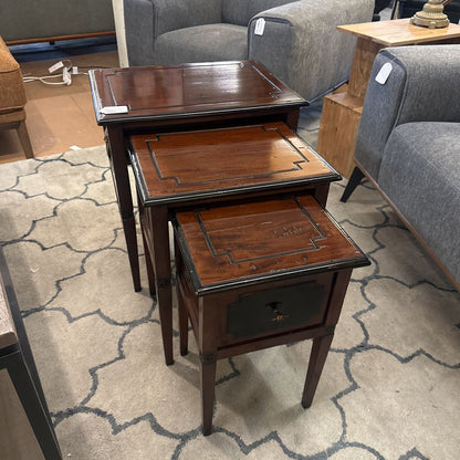 Set of three wooden nesting tables on a patterned rug with furniture in the background