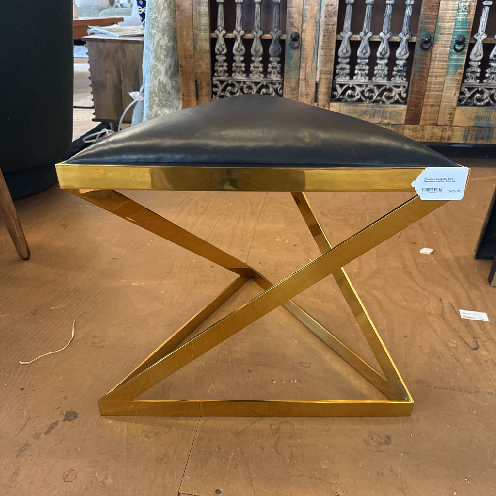 Gold metal stool with black cushion on a wooden floor