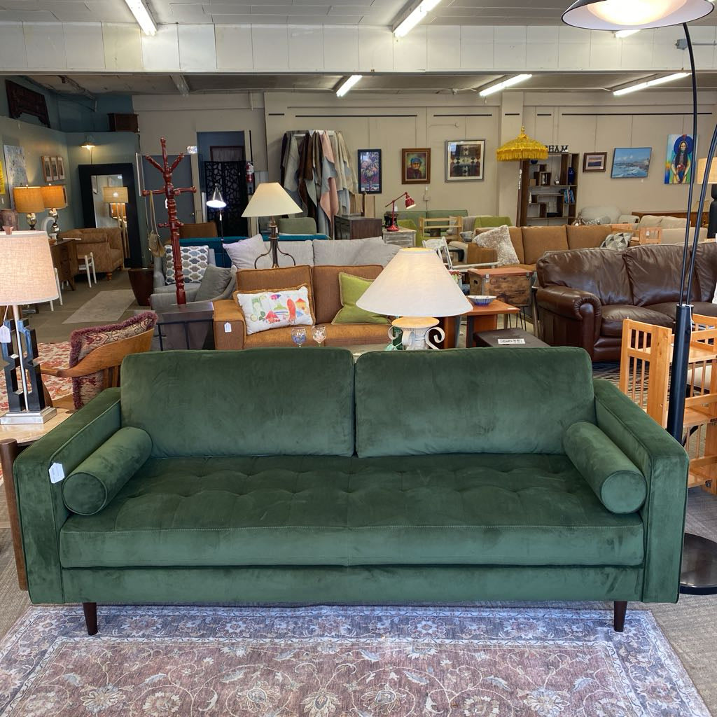 Green sofa in a furniture store with various other furniture pieces in the background.
